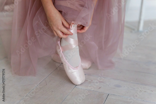 Beautiful legs of young ballerina who puts on pointe shoes at white wooden floor background, top view from above with copy space. Ballet practice. Beautiful slim graceful feet of ballet dancer. photo