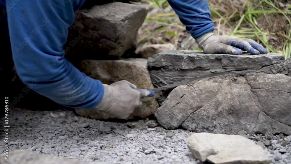 Closeup slider shot of putting mortar between large stones in a rock wall design. Closeup slider shot of putting mortar between large stones in a rock wall design.