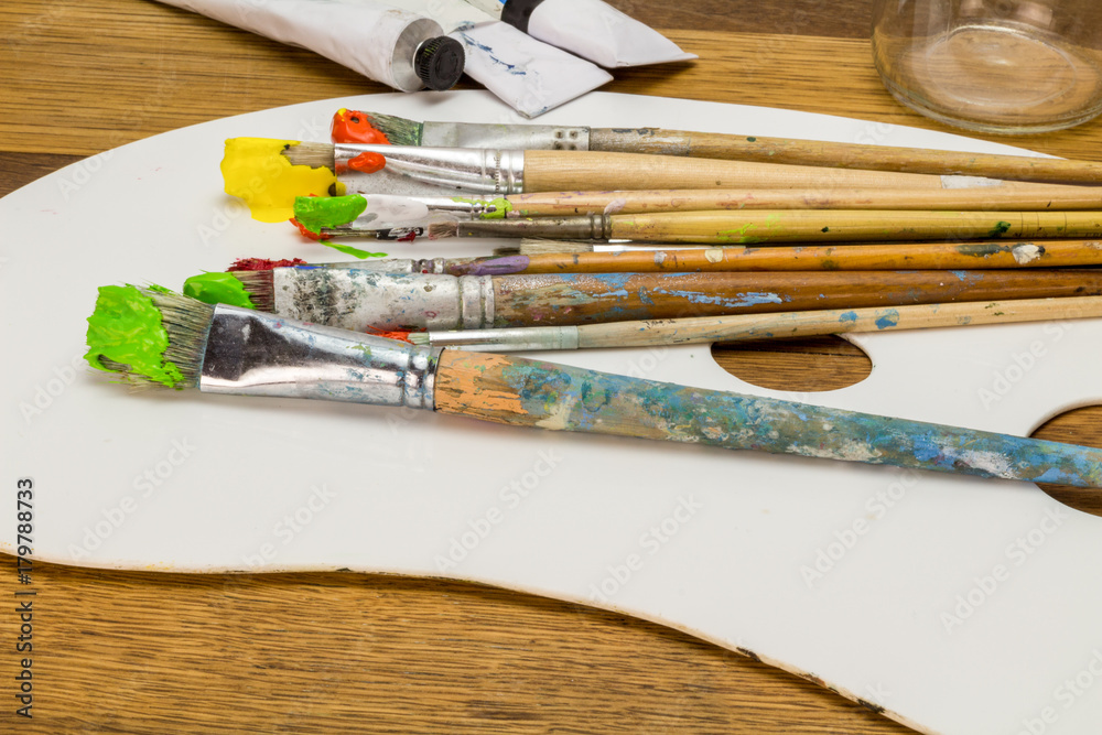 Obraz premium Art palette with colourful art brushes with orange, yellow and green paint on wooden background
