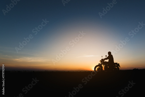 Silhouette of young man biker  and a motorcycle on the road with sunset light background