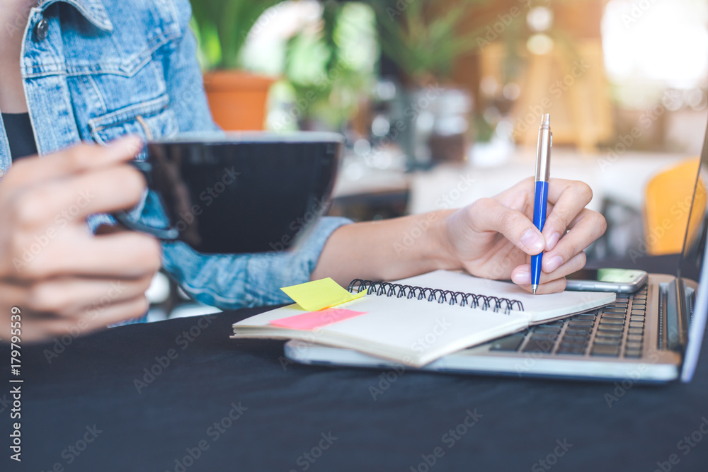 Woman hand works in a laptop computer and is writing on notepad with a pen in the office. Woman hand works in a laptop computer and is writing on notepad with a pen in the office.