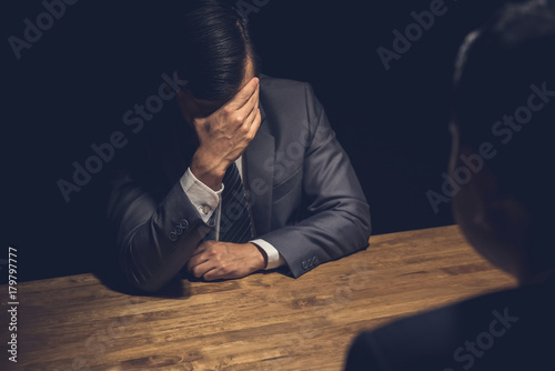 Suspect businessman displaying regret  in dark interrogation room