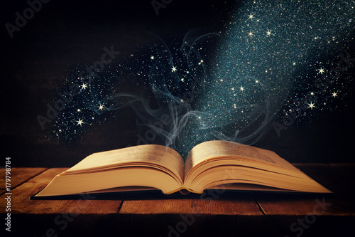Tableau sur toile image of open antique book on wooden table with glitter overlay.