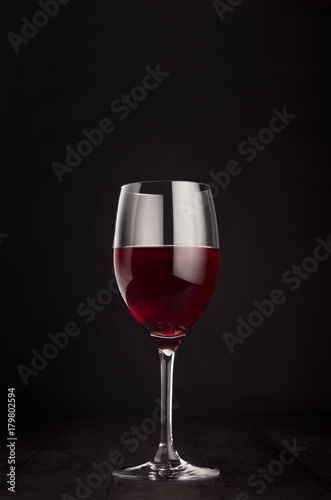 Wine glass with red wine on elegant dark black wooden background, copy space, vertical. Template for portfolio, advertising, design, branding identity, cover magazine, bar and restaurant menu.