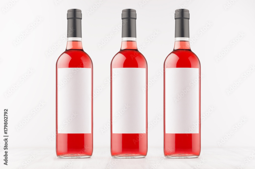 Three rose wine bottles with blank white labels on white wooden board, mock up. Template for advertising, design, branding identity. Three rose wine bottles with blank white labels on white wooden board, mock up. Template for advertising, design, branding identity.