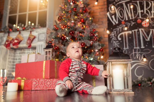 Baby first Сhristmas. Beautiful little baby boy celebrates Christmas, New Year's holidays.Cute Toddler playing and smilingnear gifts, tinsel, balls and christmas tree photo