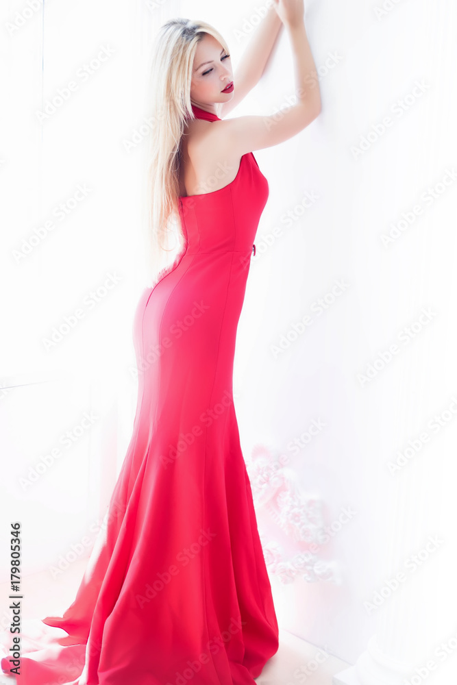 Fashion photo of beautiful lady in elegant evening dress. Studio shot.Elegant wavy hairstyle,make up,red lips.Holding trendy evening purse.Beautiful sexy blonde woman in classical background,party.
