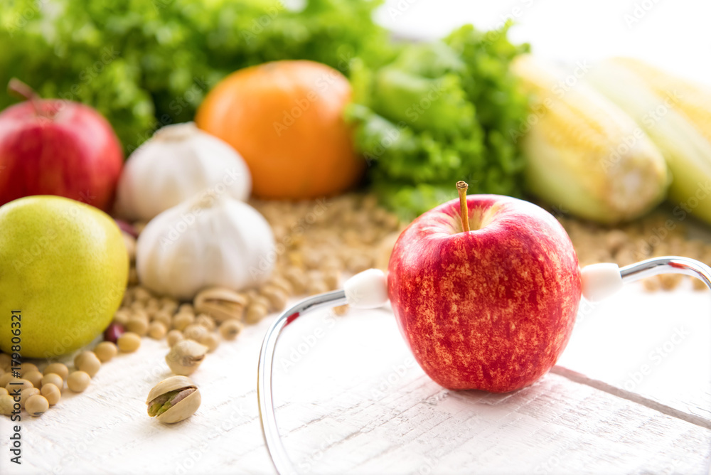 Fresh healthy red apple wearing stethoscope on white wood table Fresh healthy red apple wearing stethoscope on white wood table