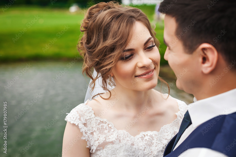 Young bride and handsome groom on wedding day. Beautiful newlyweds smiling in beautiful nature near the lake Young bride and handsome groom on wedding day. Beautiful newlyweds smiling in beautiful nature near the lake