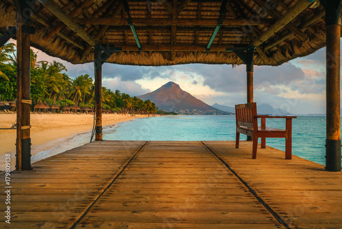 Fototapeta Naklejka Na Ścianę i Meble -  Wonderful view across the pier, on the left the tropical beach and in the background a beautiful mountain illuminated by red during sunset, Mauritius
