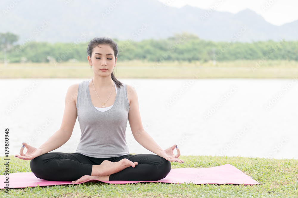 Attractive young woman exercising and sitting in yoga lotus position