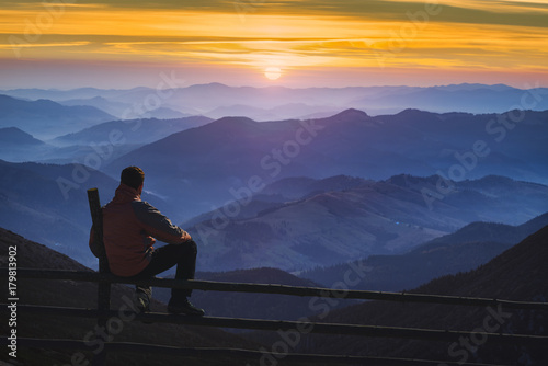 Man hiker sitting on a fence and enjoying the sunrise