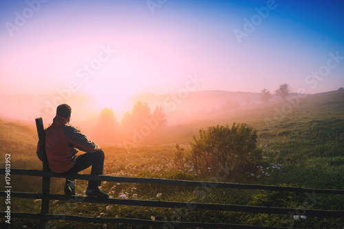 Man sitting on a wooden fence enjoy the misty morning