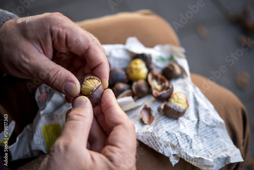 Kastanie mit den Fingern abschälen, Zeitungspapier und Kastanien am Knie, Nahaufnahme photo