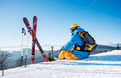 Rearview shot of a skier sitting on top of the mountain near his skiing equipment relaxing enjoying beautiful snowy mountains view people living enjoyment recreation travelling riding