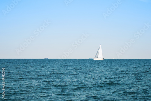 Sea lake ocean water landscape with dark waves and a lonely white yacht at the horizon on sunny day.