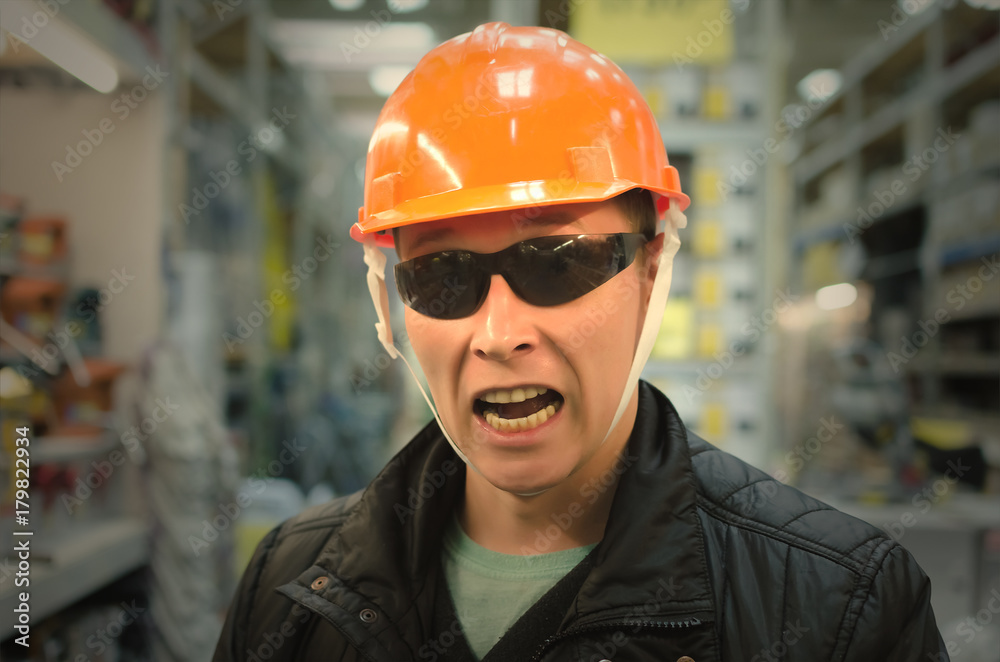 Crazy confused stumped seller of construction equipment with orange helmet above his head and in protective black glasses. Confusion. Ignorance of trade products. Crazy confused stumped seller of construction equipment with orange helmet above his head and in protective black glasses. Confusion. Ignorance of trade products.