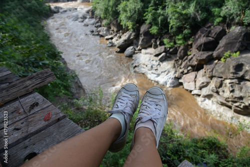 Legs of woman in white shoes and view of rapid are between mountains
