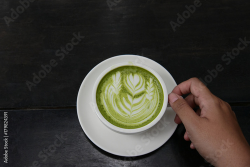 hand of woman holding a white cup of matcha green tea on black wooden background, top view