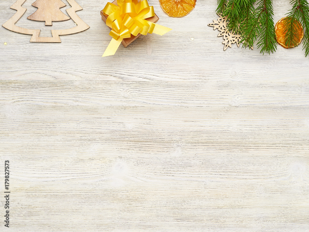 Christmas background. Small Kraft box gift with yellow bow. Fir-tree branches, wooden toys, pinecone, orange slices on a white wooden background. Christmas background. Small Kraft box gift with yellow bow. Fir-tree branches, wooden toys, pinecone, orange slices on a white wooden background.