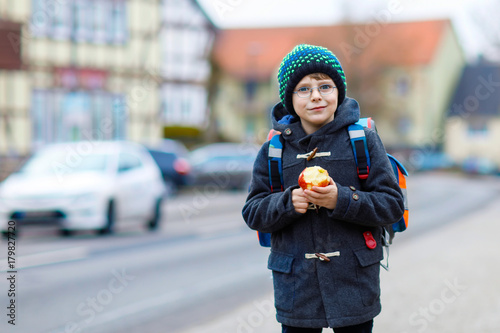 Little kid boy with eye glasses walking from the school and eating apple photo