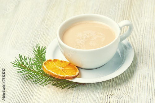 Coffee Cup cappuccino and saucer on a light wooden background decorated with fir branch and dried orange slice. Christmas morning.