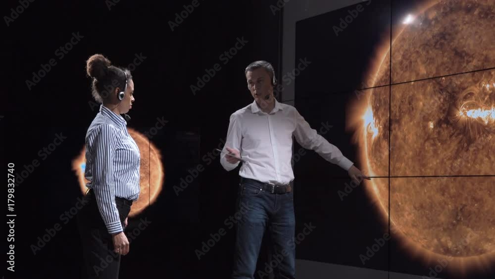 Multiracial team of scientists investigating and analyzing solar eclipse and solar activity on big screen. Elements of this image furnished by NASA.