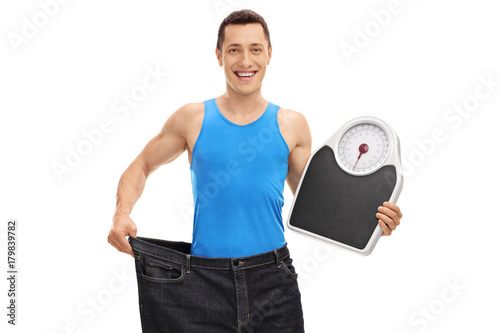 Guy in pair of oversized jeans holding a weight scale