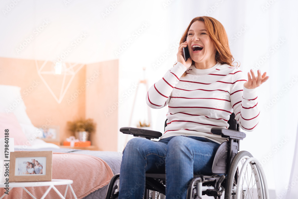 Great news. Joyful blond disabled woman smiling and talking on her phone while sitting in the wheelchair Great news. Joyful blond disabled woman smiling and talking on her phone while sitting in the wheelchair