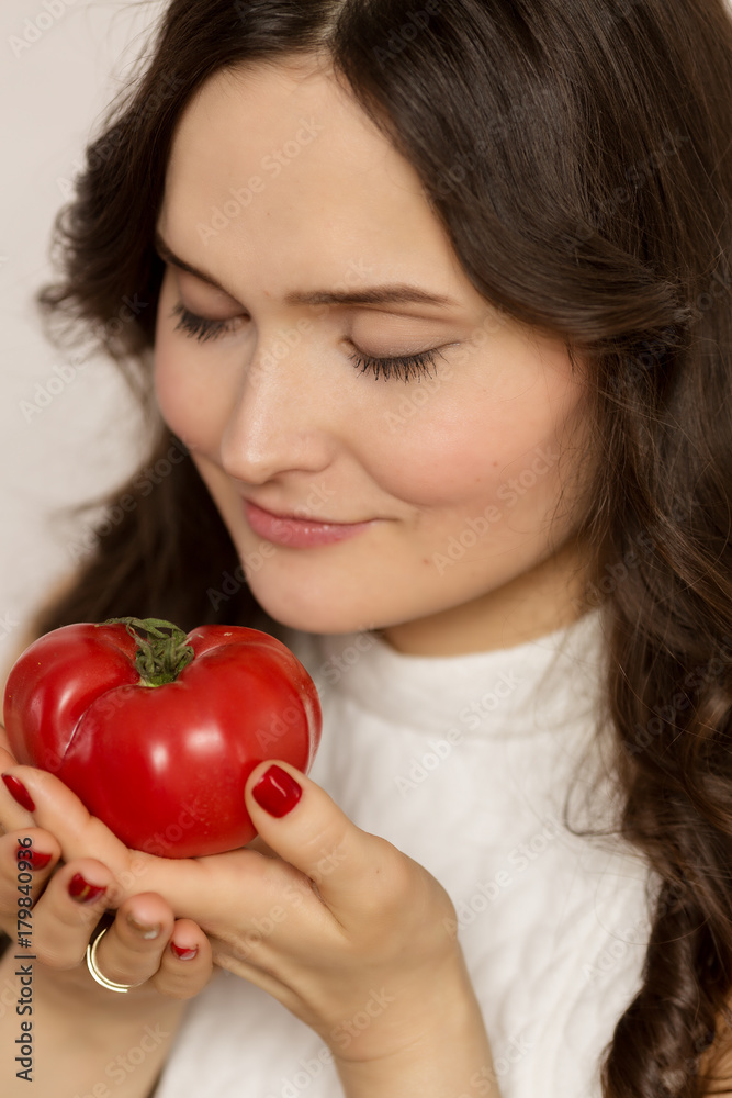 Young beautiful woman, brunette, with big tomato, close-up Young beautiful woman, brunette, with big tomato, close-up