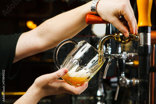 Barman pours beer into a glass goblet from the tap