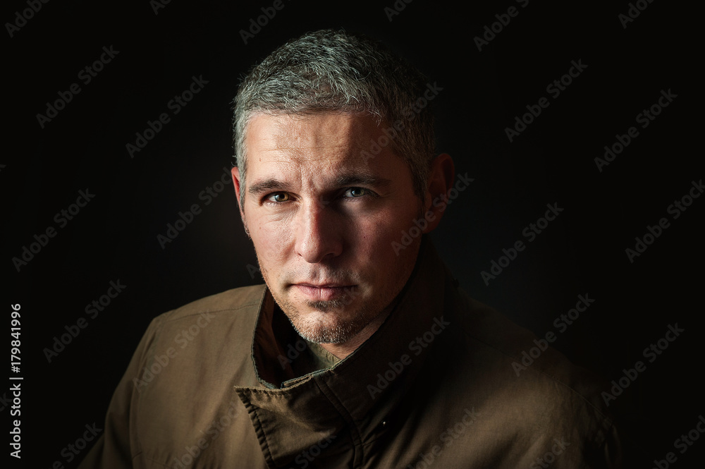 a man with jacket over black background looks into camera
