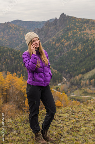A girl in a lilac jacket talking on the phone in the mountains, an autumn forest with a cloudy day, free space for text