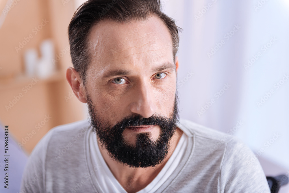 Being concentrated. Serious bearded dark-haired man of middle age having grey eyes and wearing a white shirt and thinking