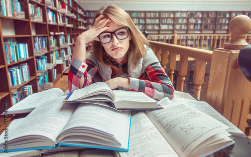 Confused and tired casual stylish student girl wears glasses studying hard with books in the library, education concept