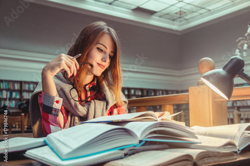 Successful casual stylish student girl wears glasses studying hard with books in the library, education concept