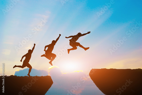 Men jump cliff sun light over silhouette 