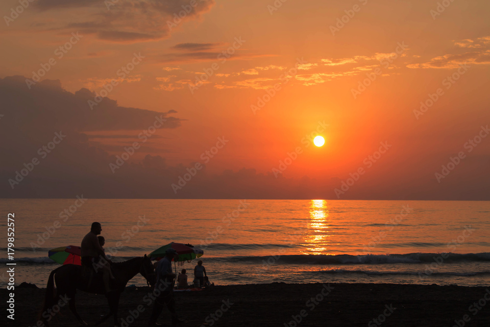 Peaceful walk along a beach. Sunny evening beach walk. The silhouettes people at the sunset background