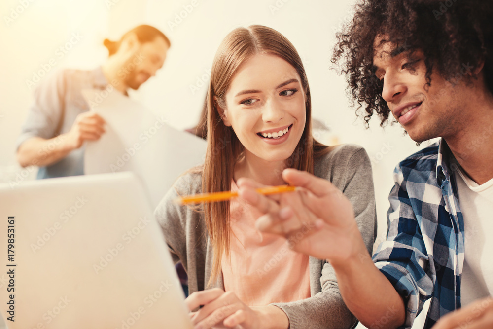 Happy hours. Motivated young smiling student looking at the screen of a laptop while her boyfriend showing his new project Happy hours. Motivated young smiling student looking at the screen of a laptop while her boyfriend showing his new project