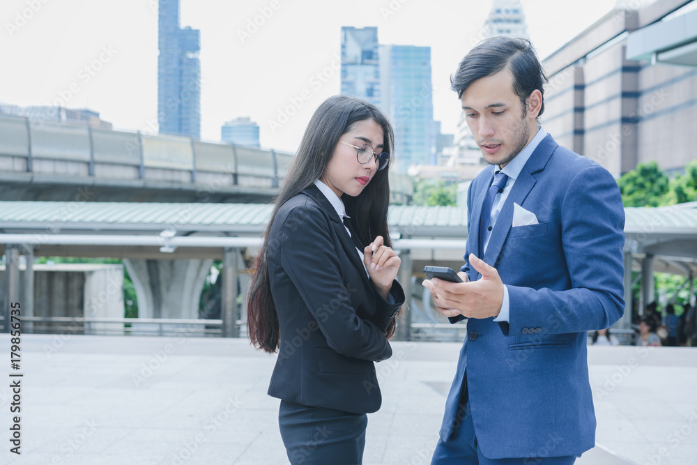 Fototapeta premium Profession businessman and businesswoman using smartphone for work outside office in cityscape background