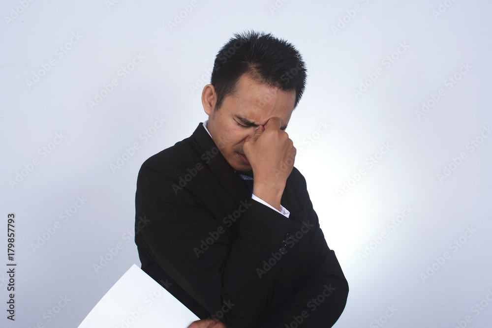 Asian businessman with headache pinching back of his nose and holding blank paper with left hand Asian businessman with headache pinching back of his nose and holding blank paper with left hand