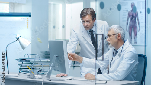Senior Doctor and His Assistant Discuss Patient s Log on Personal Computer.
