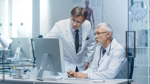 Senior Doctor and His Assistant Discuss Patient s Log on Personal Computer.