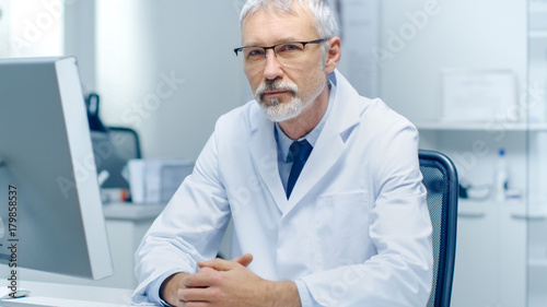 Experienced Gray Haired Senior Medical Practitioner Looking Into Camera. Portrait Shot in Modern and Light Office.