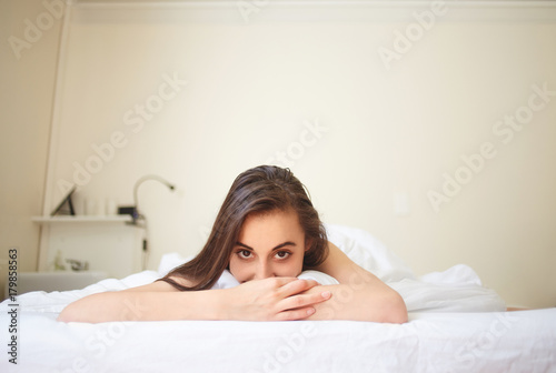 portrait of young woman lies in bed early in the morning and with a satisfied smile looks at camera