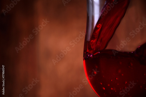 Pouring red wine into the glass against wooden rustic background