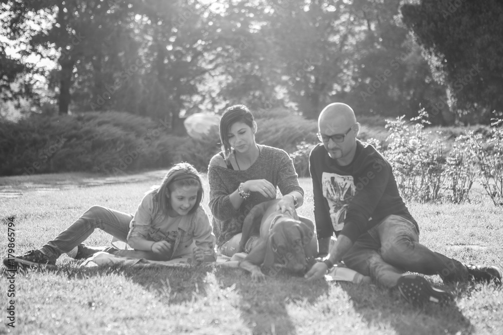 Black and white image of Beautiful gorgeous family of three playing in the park with their dog. Animal lovers. Mother, father, daughter and their dog