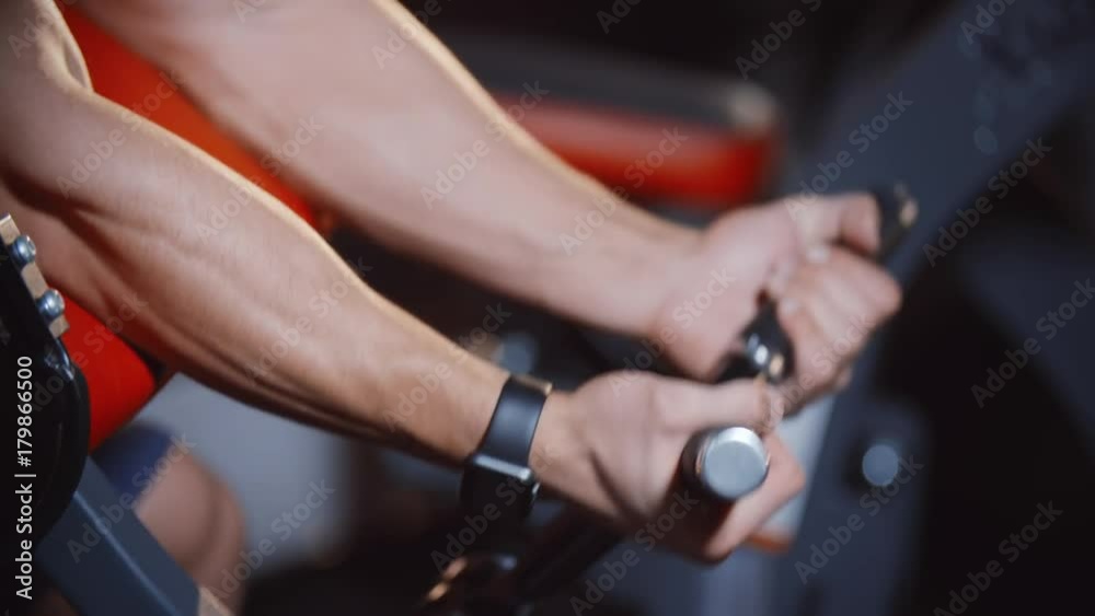 Muscular bodybuilder do biceps hand muscles workout exercise on training weight lifting apparatus in gym