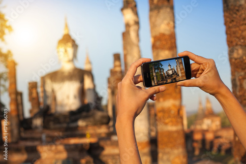 A hand taking photo of Buddha statue with smartphone, Sukhothai, Thailand