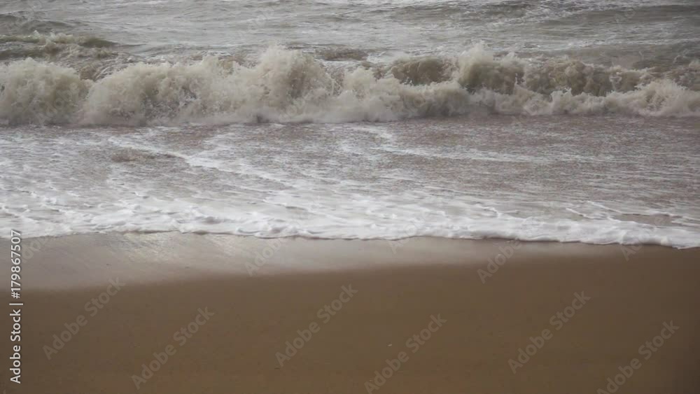 Slow mo the storm wave rolls to the sandy shore and the wind blows the foam off another wave from the sand Slow mo the storm wave rolls to the sandy shore and the wind blows the foam off another wave from the sand